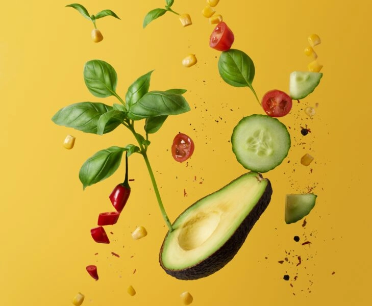 Un aguacate sobre un fondo amarillo y algunos vegetales