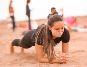 Una chica en la playa haciendo una plancha abdominal clásica, con los antebrazos apoyados en el suelo