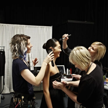 Stylists making final adjustments on female model backstage at fashion show