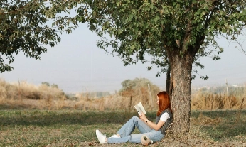 Mujer leyendo un libro sobre menopausia bajo un árbol