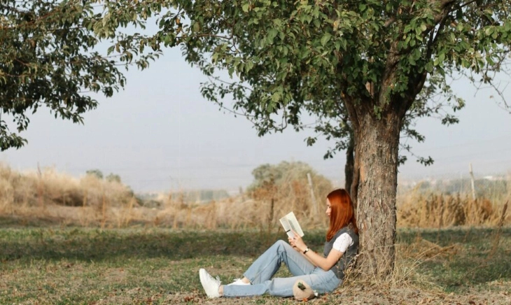 Mujer leyendo un libro sobre menopausia bajo un árbol