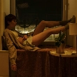 Persona sentada en el alféizar de una ventana, de noche, con gesto de insomnio y desesperación tras levantarse por dar vueltas en la cama
