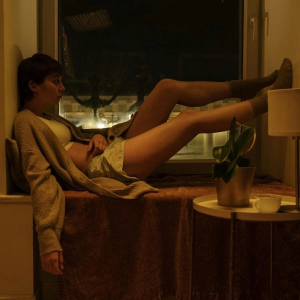 Persona sentada en el alféizar de una ventana, de noche, con gesto de insomnio y desesperación tras levantarse por dar vueltas en la cama