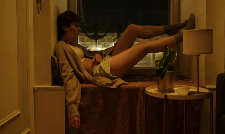 Persona sentada en el alféizar de una ventana, de noche, con gesto de insomnio y desesperación tras levantarse por dar vueltas en la cama