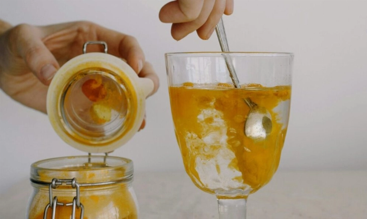Una mujer añadiendo cúrcuma, alimento imprescindible en menopausia, a un vaso.