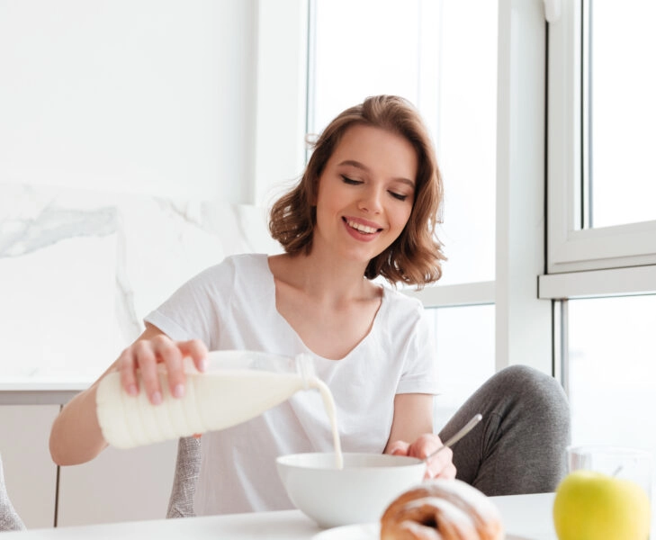 Portrait of a smiling young woman pouring milk