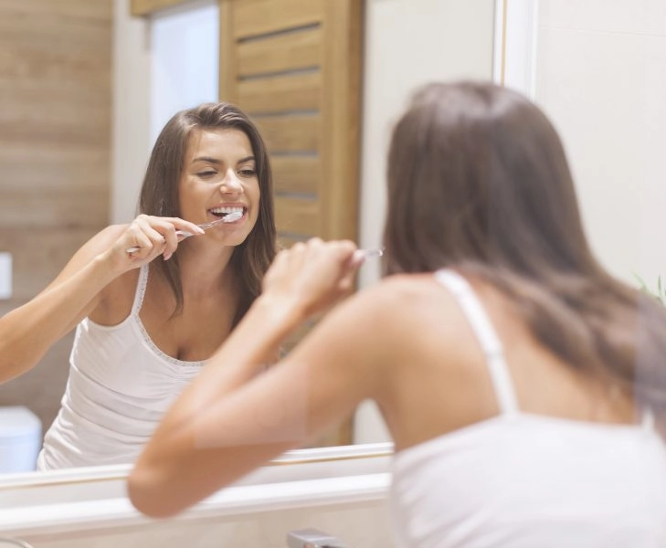 Woman brushing teeth in front of mirror. Photo taken through glass