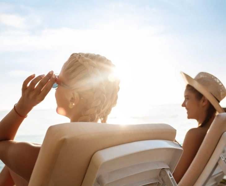 Beautiful girls in swimwear sunbathing, lying on chaises near sea.