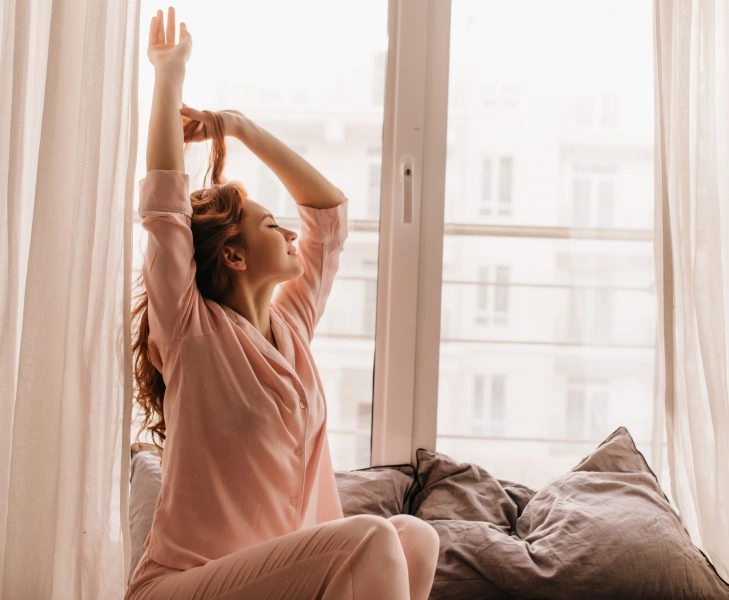 Cute female model in pink pajama enjoying morning. Pleasant ginger woman sitting on bed.