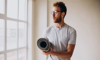 Yoga trainer standing with mat by the window