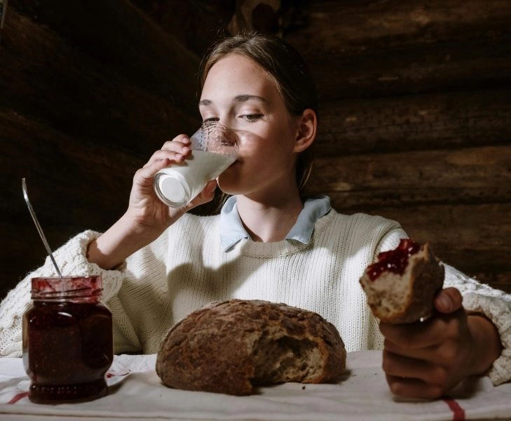 Mujer joven comiendo bollos y bebiendo un vaso de leche de noche, ejemplo de alimentos que dificultan la digestión y favorecen pesadillas