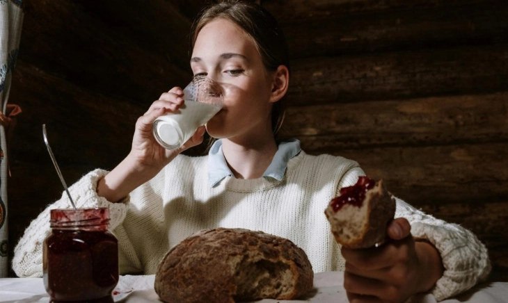 Mujer joven comiendo bollos y bebiendo un vaso de leche de noche, ejemplo de alimentos que dificultan la digestión y favorecen pesadillas