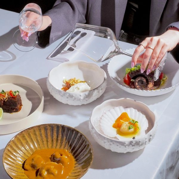 Platos de alta gastronomía saludable en mesa de restaurante, con copa de cristal vacía como maridaje sin alcohol.