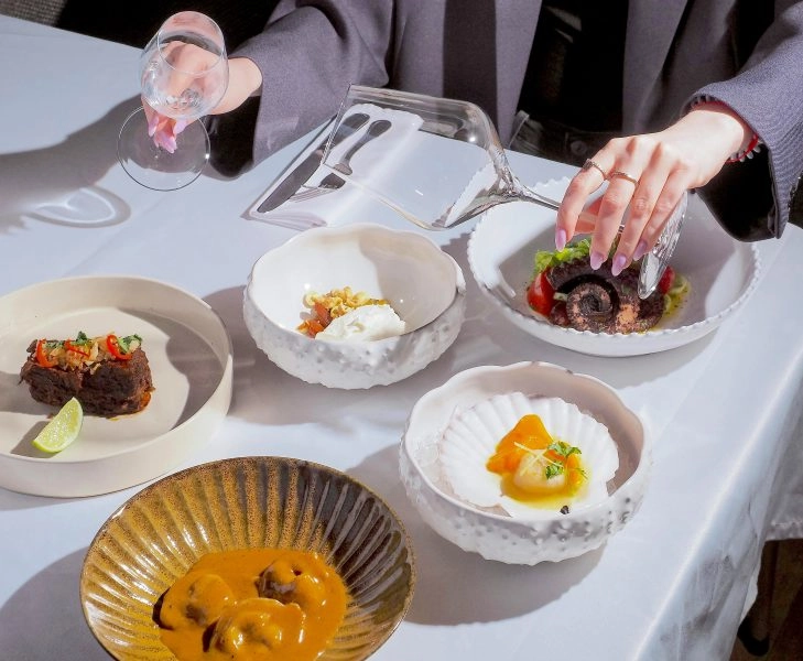 pexels-nadin-sh-78971847-15701136 (1) Platos de alta gastronomía saludable en mesa de restaurante, con copa de cristal vacía como maridaje sin alcohol.