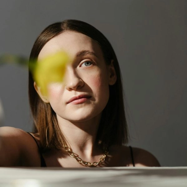 Mujer joven con gesto pensativo frente a una flor, mirando hacia un lado, símbolo de la duda interna que aparece incluso en momentos positivos.