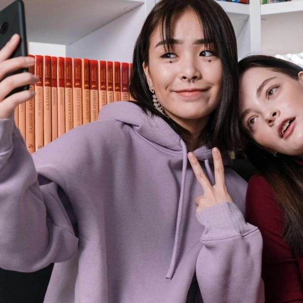 Dos chicas haciéndose un selfie; una sonríe y la otra pensando no me reconozco en las fotos, sorprendida al verse distinta