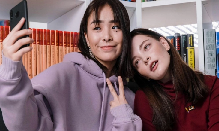 Dos chicas haciéndose un selfie; una sonríe y la otra pensando no me reconozco en las fotos, sorprendida al verse distinta