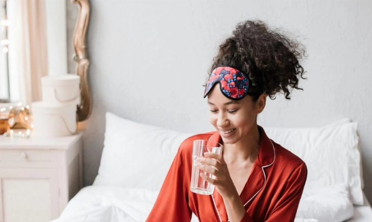 Mujer recién despierta bebiendo agua para aliviar la boca seca por la noche