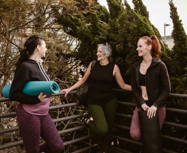Tres mujeres de mediana edad en mallas de yoga conversan relajadas antes de las charlas de ASISA WeLife Menopausia