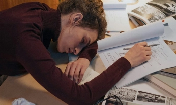 Mujer dormida en una oficina de noche, rodeada de papeles, símbolo del agotamiento por trabajar demasiadas horas