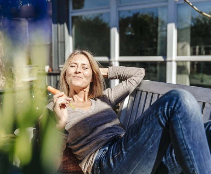 suplementación menopausia Mujer de mediana edad tomando el sol mientras muerde una zanahoria, la versión más natural de la suplementación