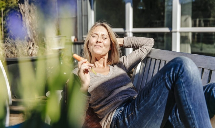 Mujer de mediana edad tomando el sol mientras muerde una zanahoria, la versión más natural de la suplementación