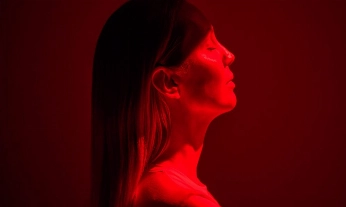 Mujer con los ojos cerrados bajo una luz roja, símbolo de bienestar y regeneración en el mejor programa de longevidad