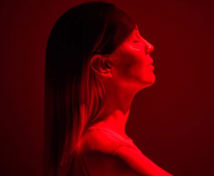 SHA programa longevidad Mujer con los ojos cerrados bajo una luz roja, símbolo de bienestar y regeneración en el mejor programa de longevidad