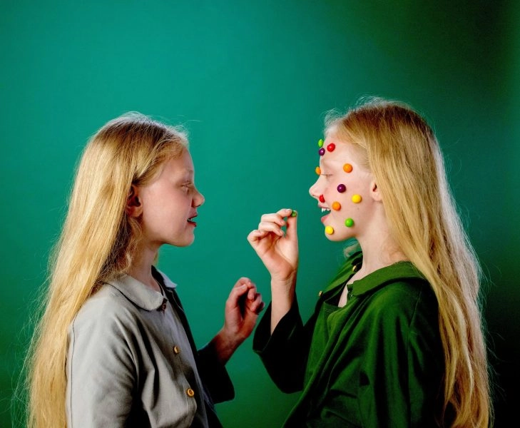 suplementos infantiles niñas jugando con caramelos de colores en el rostro, símbolo del marketing y los suplementos infantiles