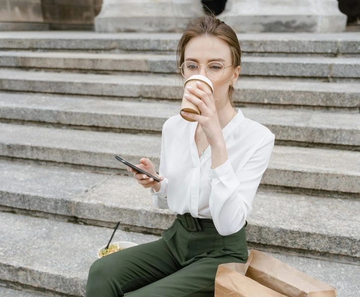 comer bien cuando no hay tiempo Persona comiendo frente a su móvil y café para llevar, símbolo de cómo intentamos comer bien cuando no hay tiempo