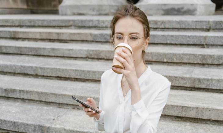 comer bien cuando no hay tiempo Persona comiendo frente a su móvil y café para llevar, símbolo de cómo intentamos comer bien cuando no hay tiempo