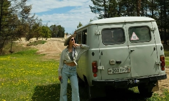 Mujer disfrutando de unas de las mejores vacaciones del mundo, junto a una furgoneta en plena naturaleza bajo un cielo azul