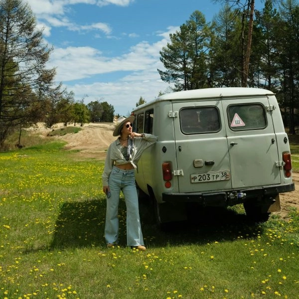 Mujer disfrutando de unas de las mejores vacaciones del mundo, junto a una furgoneta en plena naturaleza bajo un cielo azul