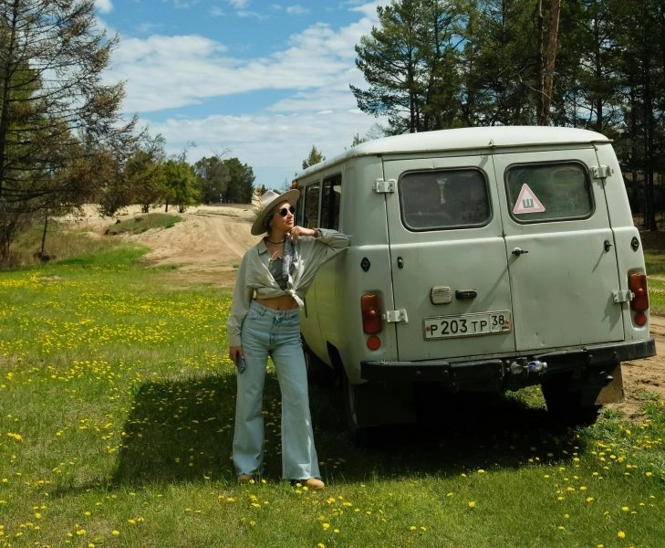 Mujer disfrutando de unas de las mejores vacaciones del mundo, junto a una furgoneta en plena naturaleza bajo un cielo azul
