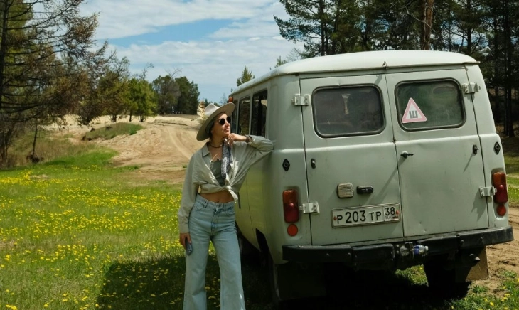 mejores vacaciones del mundo Mujer disfrutando de unas de las mejores vacaciones del mundo, junto a una furgoneta en plena naturaleza bajo un cielo azul