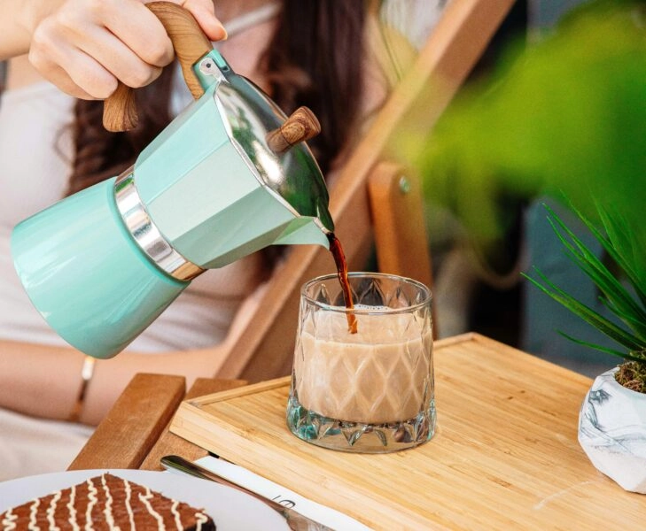 postbióticos Mujer sirviendo café junto a un bollito con chocolate, ejemplo de hábitos poco convencionales que estimulan los postbióticos