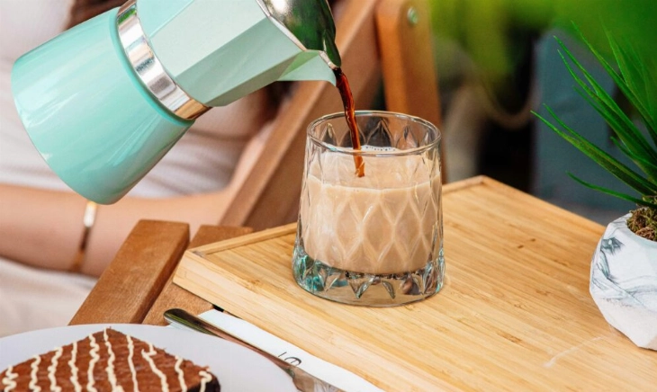 Mujer sirviendo café junto a un bollito con chocolate, ejemplo de hábitos poco convencionales que estimulan los postbióticos