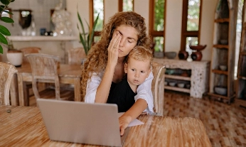 mujer cansada intenta eliminar el estrés mientras trabaja con su hijo pequeño en brazos