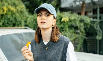 Mujer comiendo snacks frente a un coche, simbolizando cómo los superestímulos de la industria alimentaria se basan en la manipulación para crear adicciones.