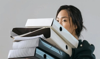 Mujer cargando una pila de archivadores en la oficina, reflejo del burnout y de la tensión entre trabajo y satisfacción laboral