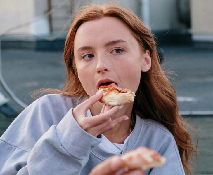 Persona comiendo al aire libre en una ciudad; la escena ilustra cómo el entorno urbano —poco verde, ruido y dependencia del coche— condiciona hábitos y puede favorecer el aumento de peso