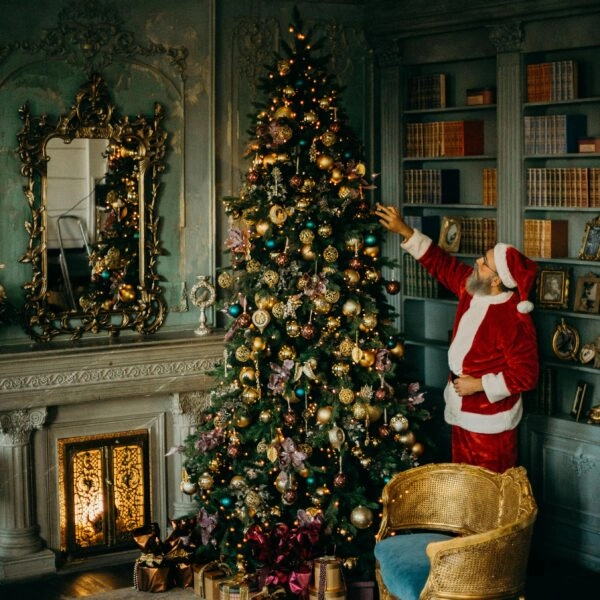 Hombre vestido de Papá Noel decorando un árbol de Navidad en un salón clásico, imagen que refleja la búsqueda de cómo ser feliz en Navidad sin idealizarla