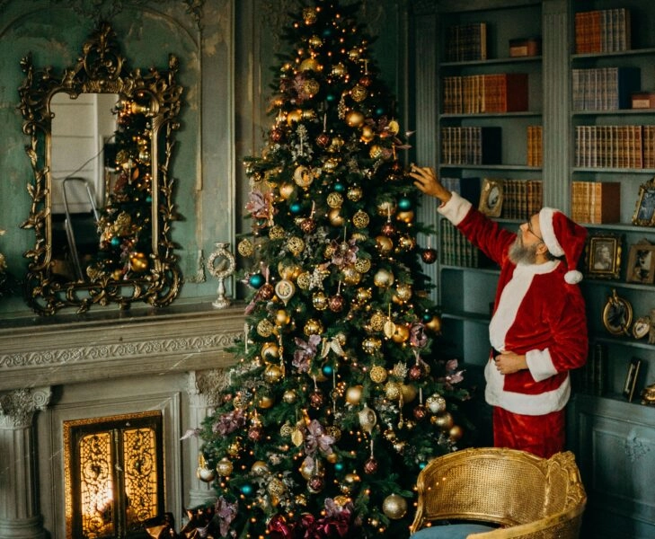 Hombre vestido de Papá Noel decorando un árbol de Navidad en un salón clásico, imagen que refleja la búsqueda de cómo ser feliz en Navidad sin idealizarla