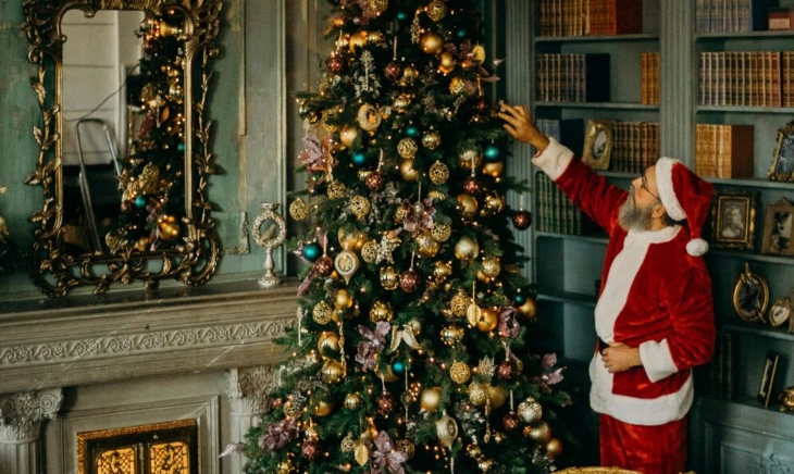 Hombre vestido de Papá Noel decorando un árbol de Navidad en un salón clásico, imagen que refleja la búsqueda de cómo ser feliz en Navidad sin idealizarla