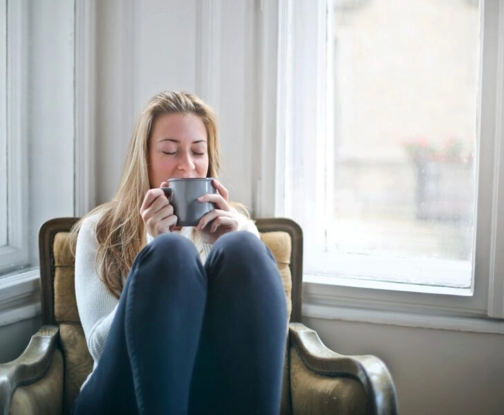 Mujer relajándose con una taza de té junto a una ventana, simbolizando el ritual del tea cycling en menopausia
