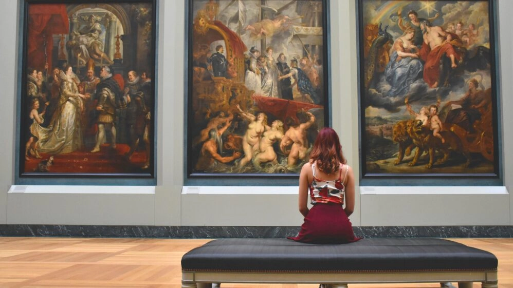Mujer sentada frente a grandes pinturas en un museo, imagen que refleja los beneficios del museo para la mente y la meditación
