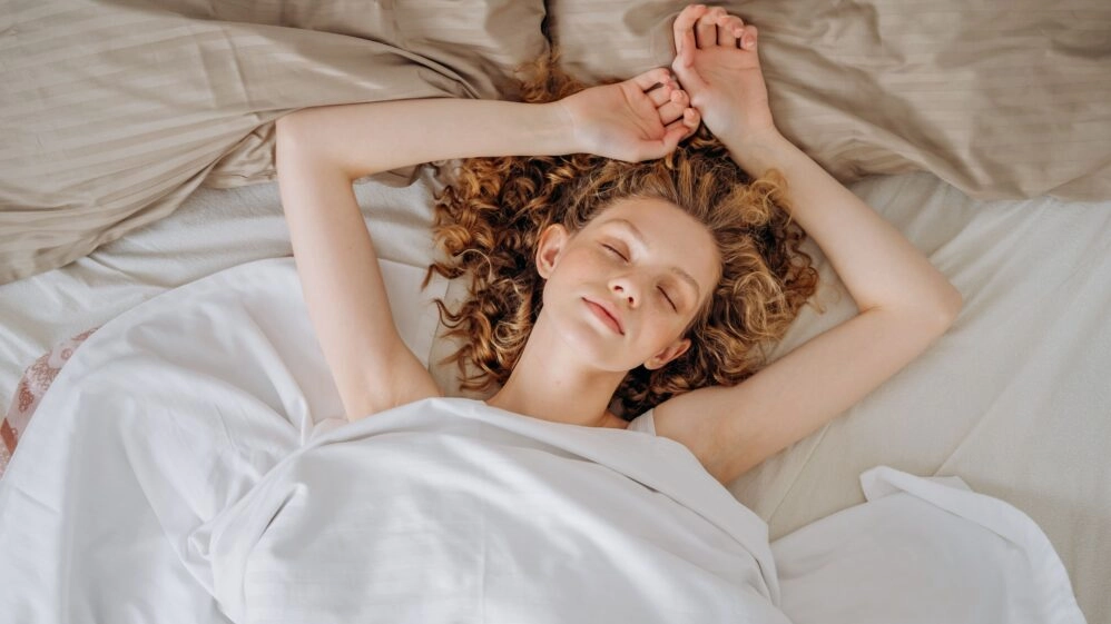 Mujer durmiendo plácidamente en la cama, en una escena que evoca el descanso reparador y la importancia del sueño para la salud.
