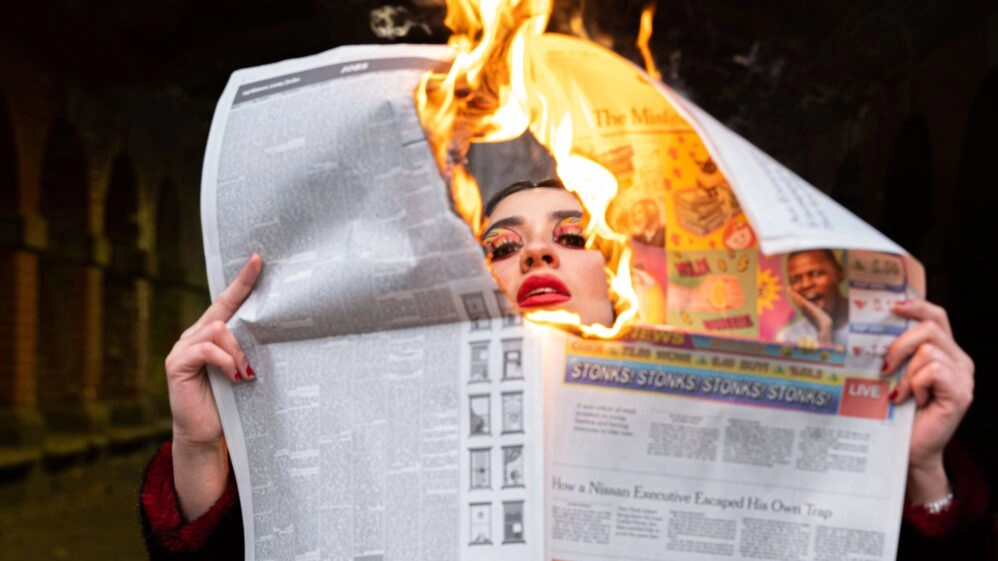 Mujer con expresión de calor y un periódico en llamas alrededor de la cara, representando un sofoco