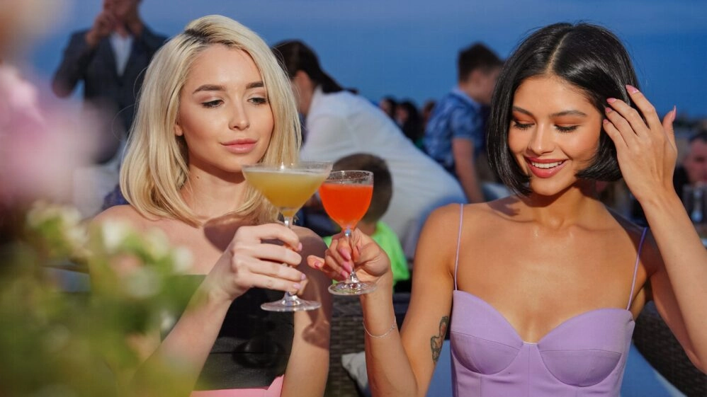 Amigas brindando con bebidas alcohólicas de aspecto refrescante durante el verano, contexto relacionado con el efecto deshidratante del alcohol cuando hace calor